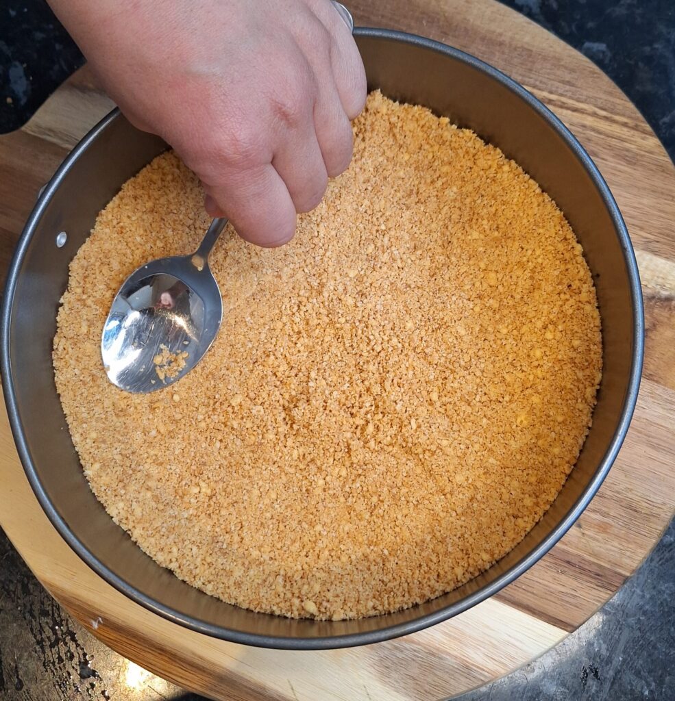 Flattening biscuit base into cake tin